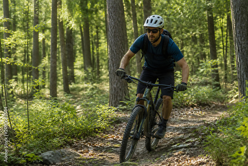 A man wearing a helmet and cycling gear rides a mountain bike on a dirt trail through a dense forest.