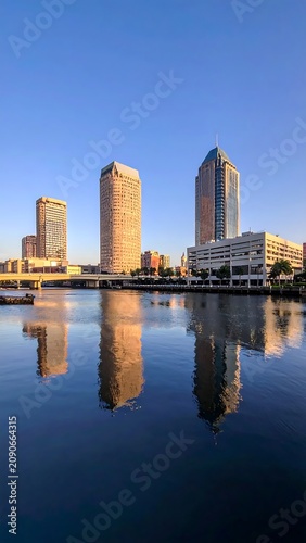 Sunlit Downtown Skyscrapers Reflecting on Calm River at Blue Hour