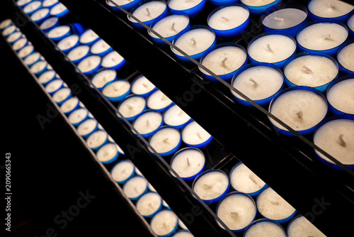 Rows of unlit red and blue votive candles on a stand. High angle close-up shot of white wax and wicks in glass cups, creating a repeating pattern.