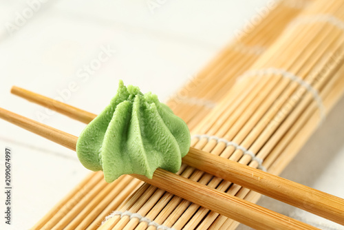 Photography Chopsticks with wasabi paste and bamboo mat on white tile background, closeup