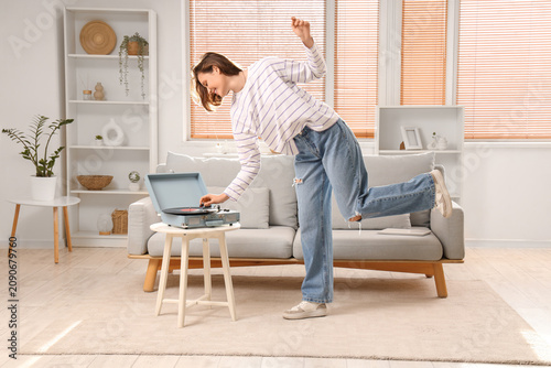 Young woman with record player dancing at home