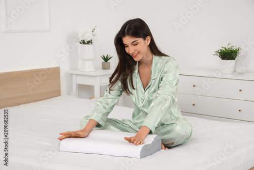 Young woman in pajamas with cozy orthopedic pillow on bed at home