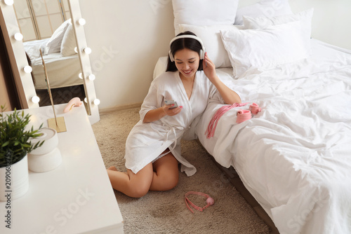 Young Asian woman in headphones with mobile phone and sex toys sitting on flo...