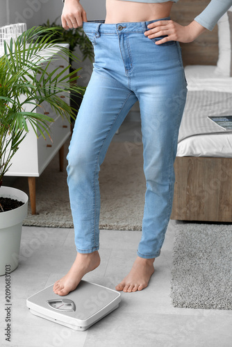 Young woman in loose jeans measuring weight at home. Diet concept