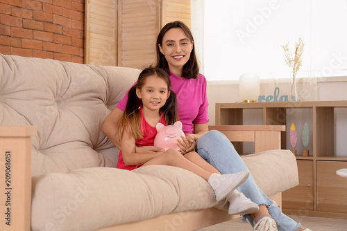Little girl with piggy bank and her mother at home