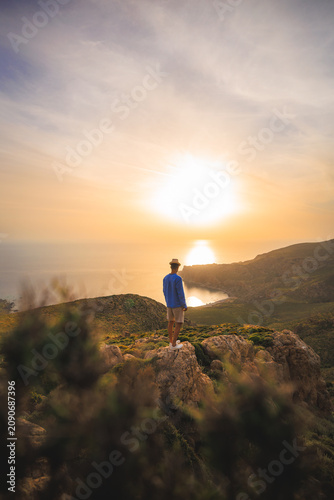 Lone traveler watches sunset above the western coast of Crete, surrounded by rocky hills