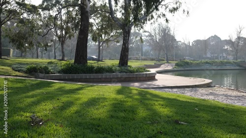 A scenic public parkland and lakeside reserve features a lush green grass lawn within the master-planned estate of Sanctuary Lakes, traffic in background. Suburb of Point Cook, Melbourne, Australia. 