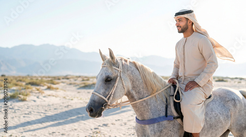Arab man riding horse in traditional thobe in desert landscape during daytime  
