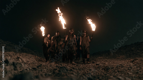 Group of ancient warriors with torches walk at night across rough terrain