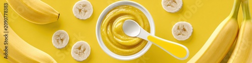 Banana puree baby food in a bowl with fresh banana slices on yellow background.