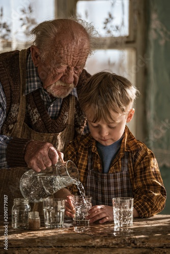 Grandfather pouring fresh water from bottle into glass for his cute little grandson.