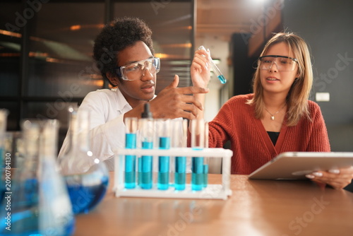 Obraz na plátně Two science students in a chemistry laboratory compares two test tubes of blue l