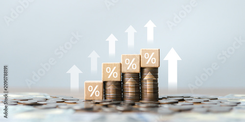 Foto A wooden block image with percentage (%) symbols stacked on a pile of coins, with an upward-pointing arrow, reflects effective financial planning and increasing interest