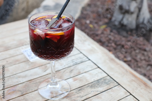 Refreshing cocktail in a crystal glass with ice and citrus garnishes on a rustic wooden table outdoors in a garden setting