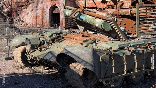 Obraz na plátne Close-up of a destroyed tracked armored vehicle showing a broken caterpillar track, torn rubber mudguards, and a rusted metal hull under bright sunlight