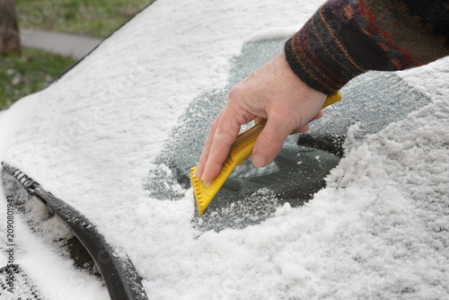 Winter scene, human hand scraping ice from windshield of car