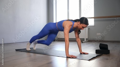 Motivated active sporty fit woman practicing mountain climber exercise, improving balance, agility, coordination, strength, flexibility and blood circulation during workout in fitness studio.