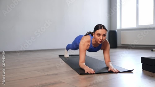Determined elegant woman in activewear practicing yoga plank pose exercise, strengthening spine, rhomboids, trapezius and abdominal muscles while working out in health club.