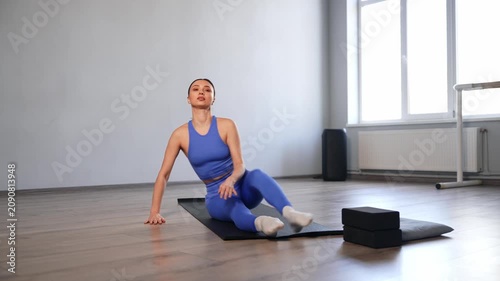 Active sporty fit beautiful woman doing seated forward bend exercise paired with front splits on yoga mat, stretching and flexing lower back , spine and leg muscles during workout in gym.