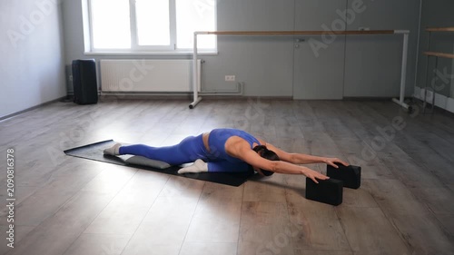 Elegant pretty sporty fit flexible woman performing sleeping swan yoga pose with blocks on fitness mat, stretching hips, glutes, psoas, and thighs while doing sports training in health club