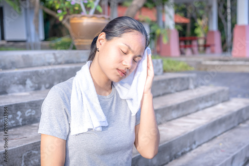 Fotografie A young Asian woman in sportswear wiping sweat with a towel while resting on outdoor stairs after a workout, authentic healthy and active recovery lifestyle photography