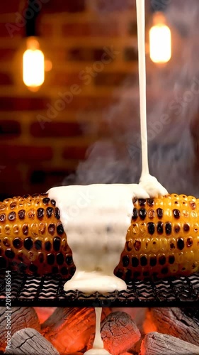 Roasted corn on the cob being smothered in butter on a grill