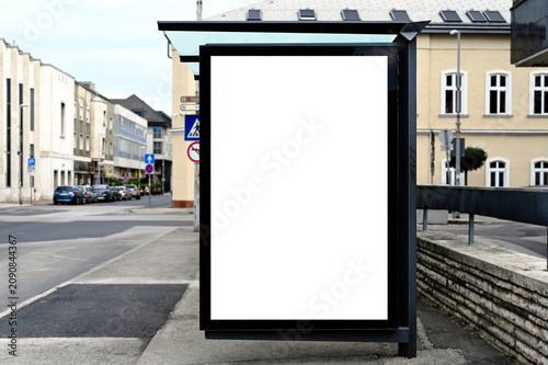bus shelter at a busstop. blank billboard ad display. empty white lightbox sign. glass and aluminum frame structure. city transit station. bench inside. urban street setting. outdoor advertising