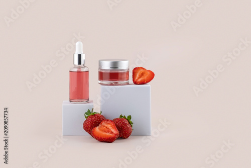containers for skin care products on a white podium and fresh strawberries on a pink background