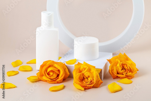 containers for skin care products and yellow rose flowers on a beige background next to geometric shapes