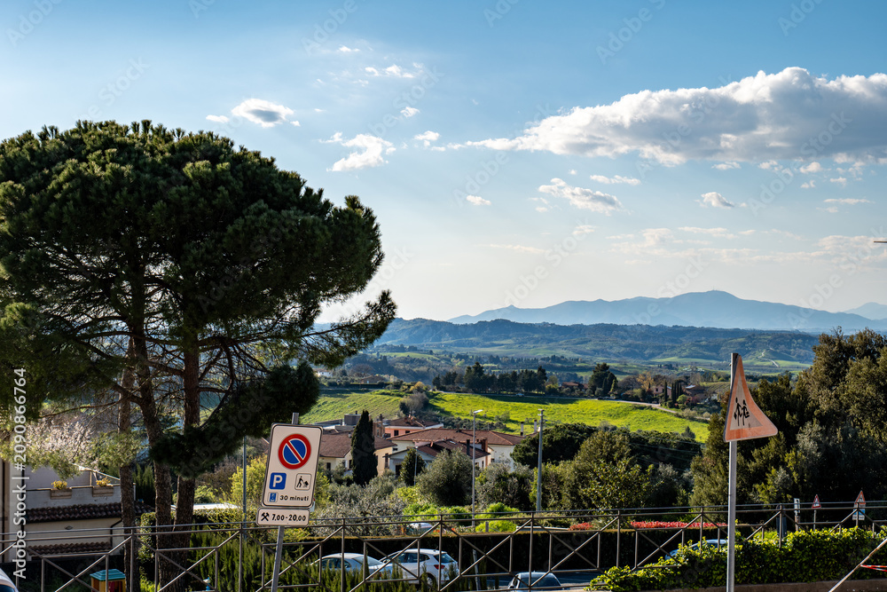Obraz premium Panoramic view of the Tuscan countryside with a roadside overlook, distant hills, and a wide valley under a bright sky. The scene captures the beauty of rural Italy.