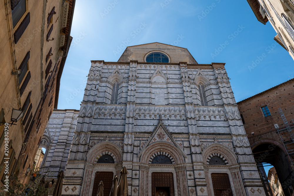 Fototapeta premium Low-angle view of Siena Cathedral with ornate white marble facade and decorative details. The perspective highlights the monument’s craftsmanship and grandeur.