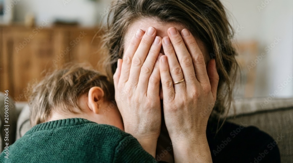 Fototapeta premium Tired mother covering face with hands, in indoor possibly living room, with hands, fingers, green sweater, with fabric sweater, skin texture, from a over-the-shoulder view perspective.