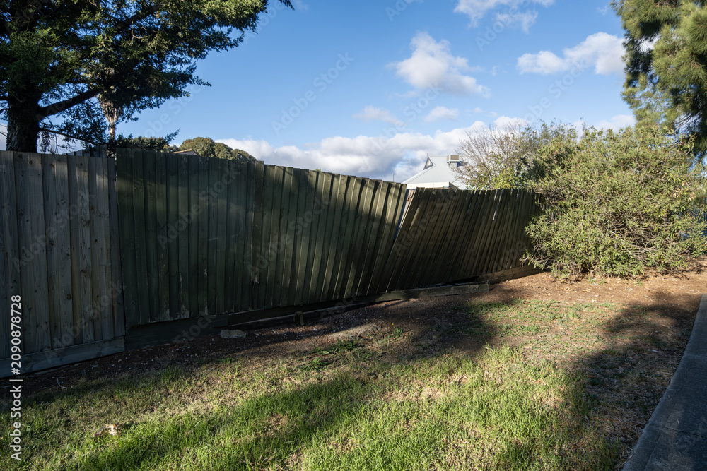 Fototapeta premium Leaning weathered timber paling fence or damaged wooden fencing in suburban Australia. Aging residential boundary fence. Concept of property maintenance, decay, and home improvement