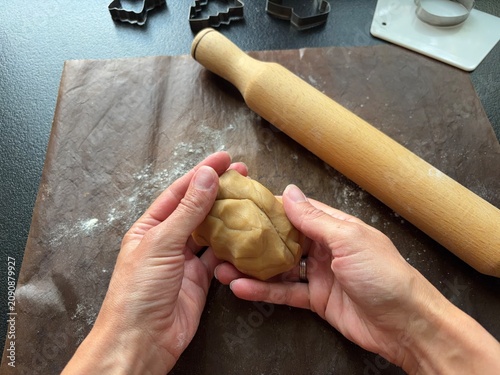 hands holding a ball of cookie dough with a rolling pin and cutters on a baking mat