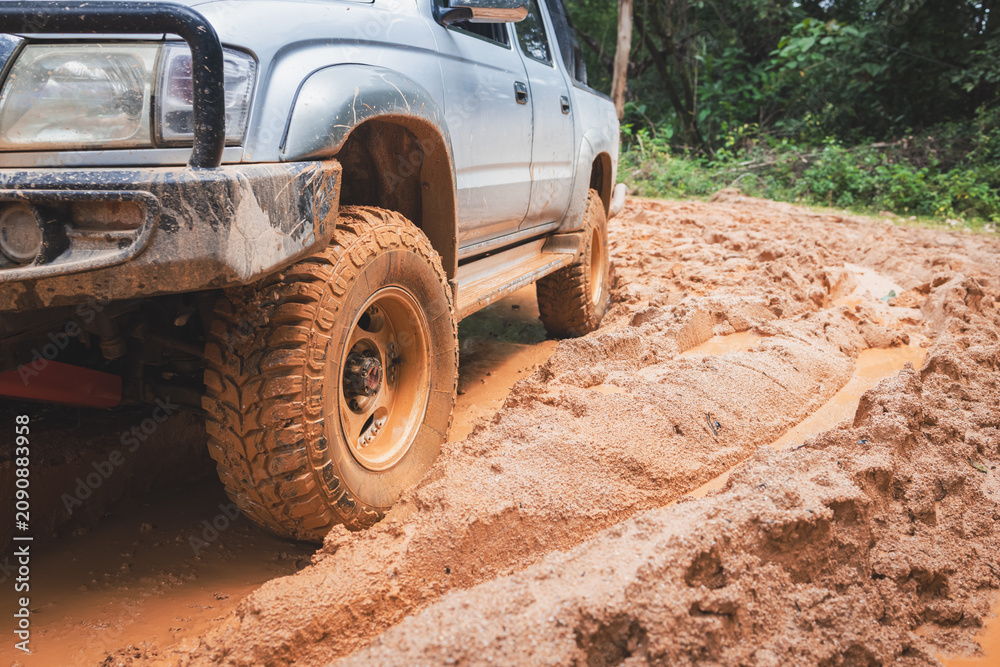 Obraz premium Aggressive mud tires gripping a wet offroad trail as the wheels throw mud in every direction. 4x4 truck, wheel spin, off-road adventure, overlanding, rough terrain, outdoor exploration.