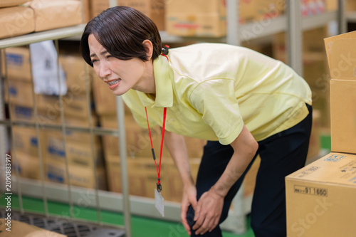 Foto 倉庫作業でひざの痛みを訴える女性スタッフ
