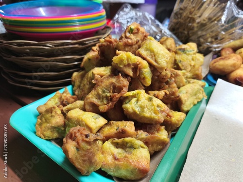 A pile of various traditional Indonesian deep-fried snacks, known as gorengan, including fried tofu, tempeh, and vegetable fritters, neatly arranged on a tray at a street food stall.