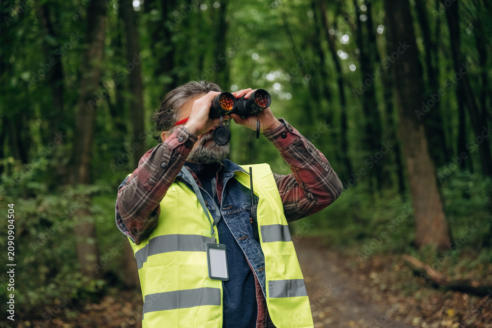 Obraz premium Professional binoculars in hands. Senior forest ecologist is working in the woods. In the uniform