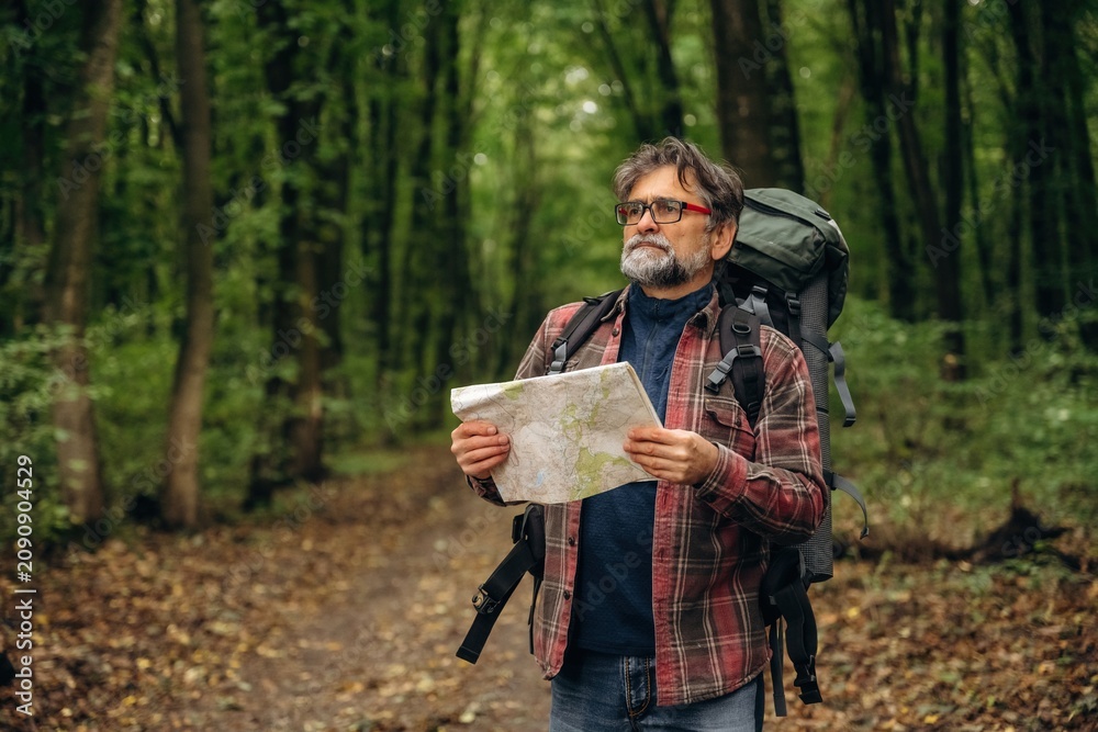 Obraz premium Paper map is in hands. Hiking experience, senior man is in the forest at daytime