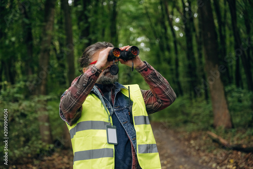 Professional binoculars in hands. Senior forest ecologist is working in the woods. In the uniform