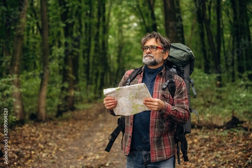 Paper map is in hands. Hiking experience  senior man is in the forest at daytime