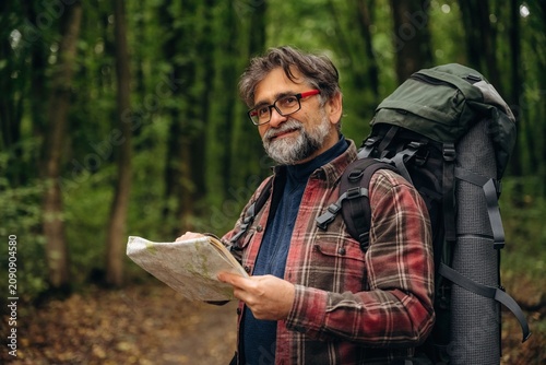 Navigation conception  with map. Hiking experience  senior man is in the forest at daytime