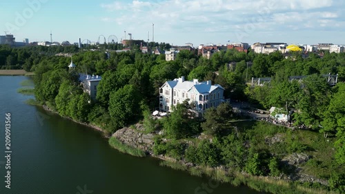 Aerial drone view of Art Cafe Terrace located by Töölönlahti Bay in Helsinki, Finland. Beautiful urban waterfront scenery featuring the café terrace, surrounding nature, and Helsinki city landscape.