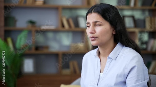 Allergic woman sneezes and wipes her nose with a handkerchief. Girl is sick with cold or flu. Unhealthy female suffering from seasonal allergies sitting on sofa in living room at home. Close up.