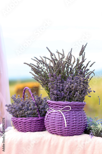 
Fresh lavender bouquets in handwoven purple baskets on a rustic table outdoors. Romantic countryside still life with blooming flowers, soft natural light, copy space, summer harvest and floral decor.