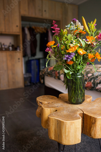 Bright mixed wildflower bouquet in glass vase on rustic wooden table in cozy bedroom. High quality photo