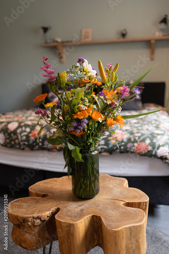 bouquet of flowers arranged in a green glass vase on a wooden shelf in a cozy bedroom with a floral . High quality photo