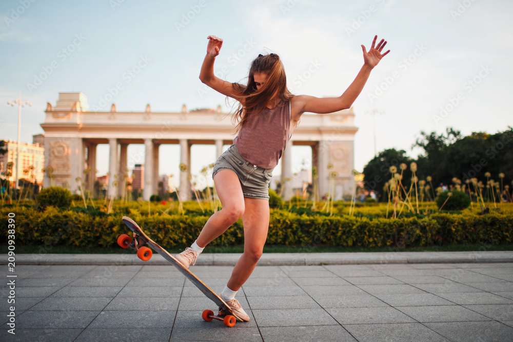 Obraz premium Young woman riding on the longboard skateboard in the park