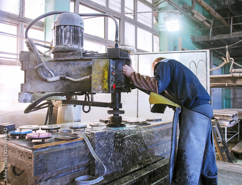 Worker operates machine at a workshop for stone processing in a busy factory during daylight hours