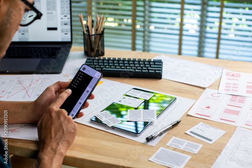 UX UI designer testing prototype on a phone, working on wireframes for a website and mobile app prototype, in concept of website and mobile application design concept.